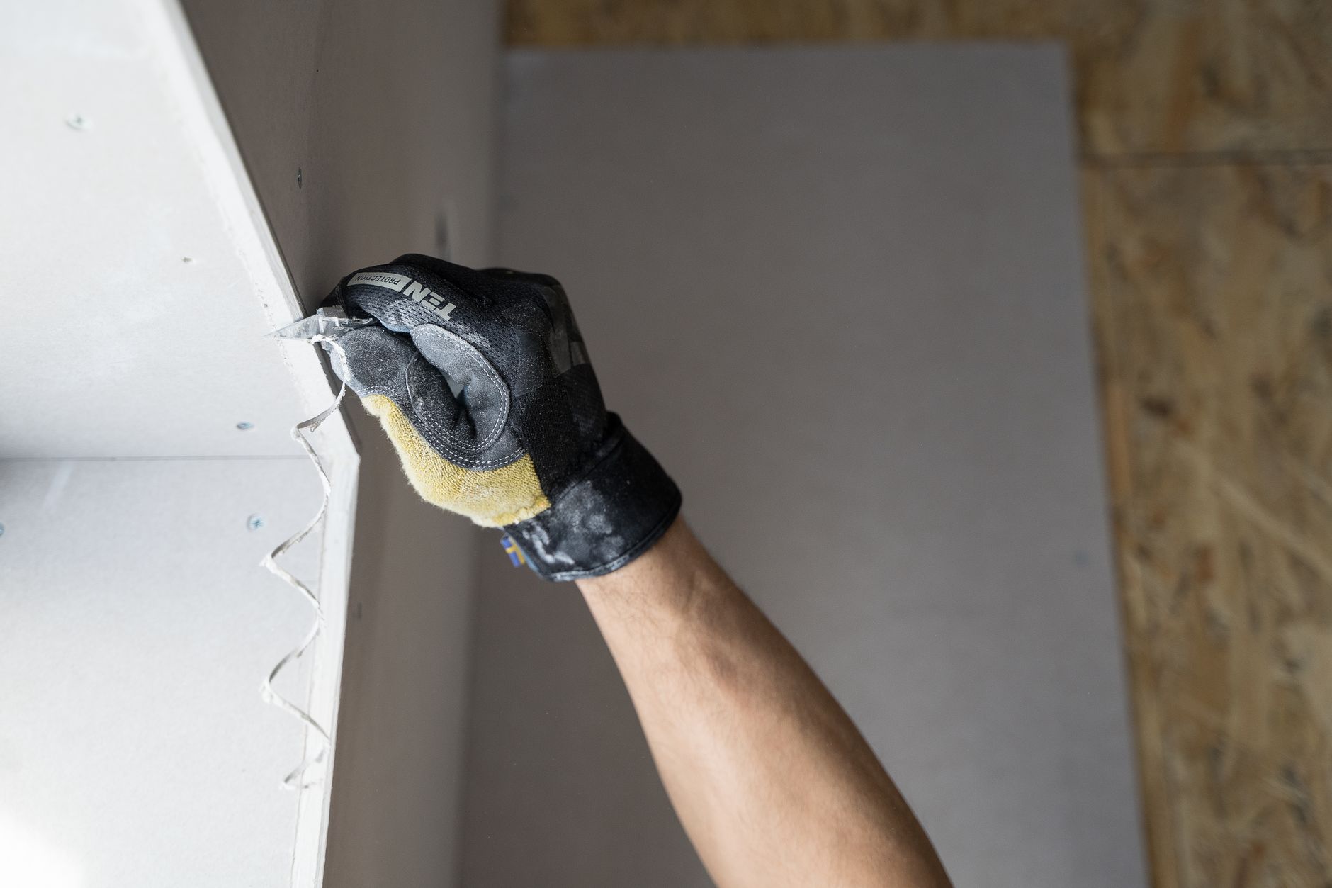 Close-up of a gloved hand applying plaster to a wall indoors in Riverside, CA